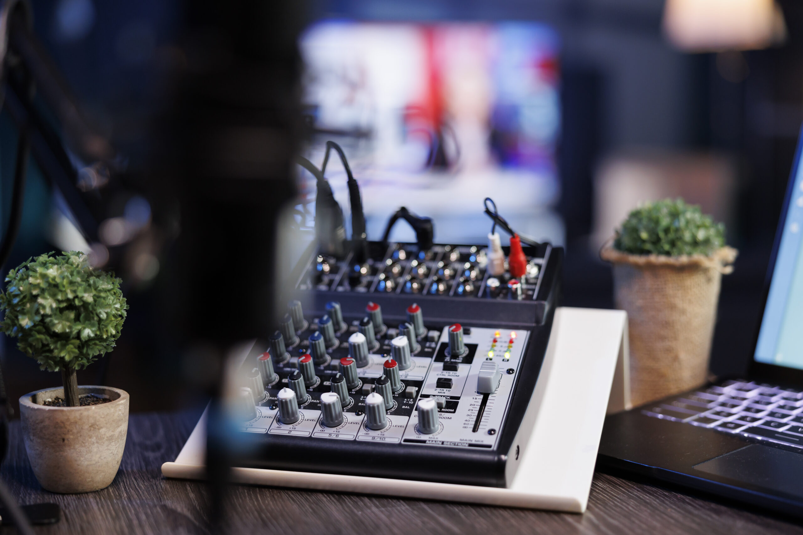 Selective focus on laptop keyboard and audio mixer knobs on a podcasting desk in the home studio. Detailed view of buttons on professional sound equipment used for live internet broadcasts.